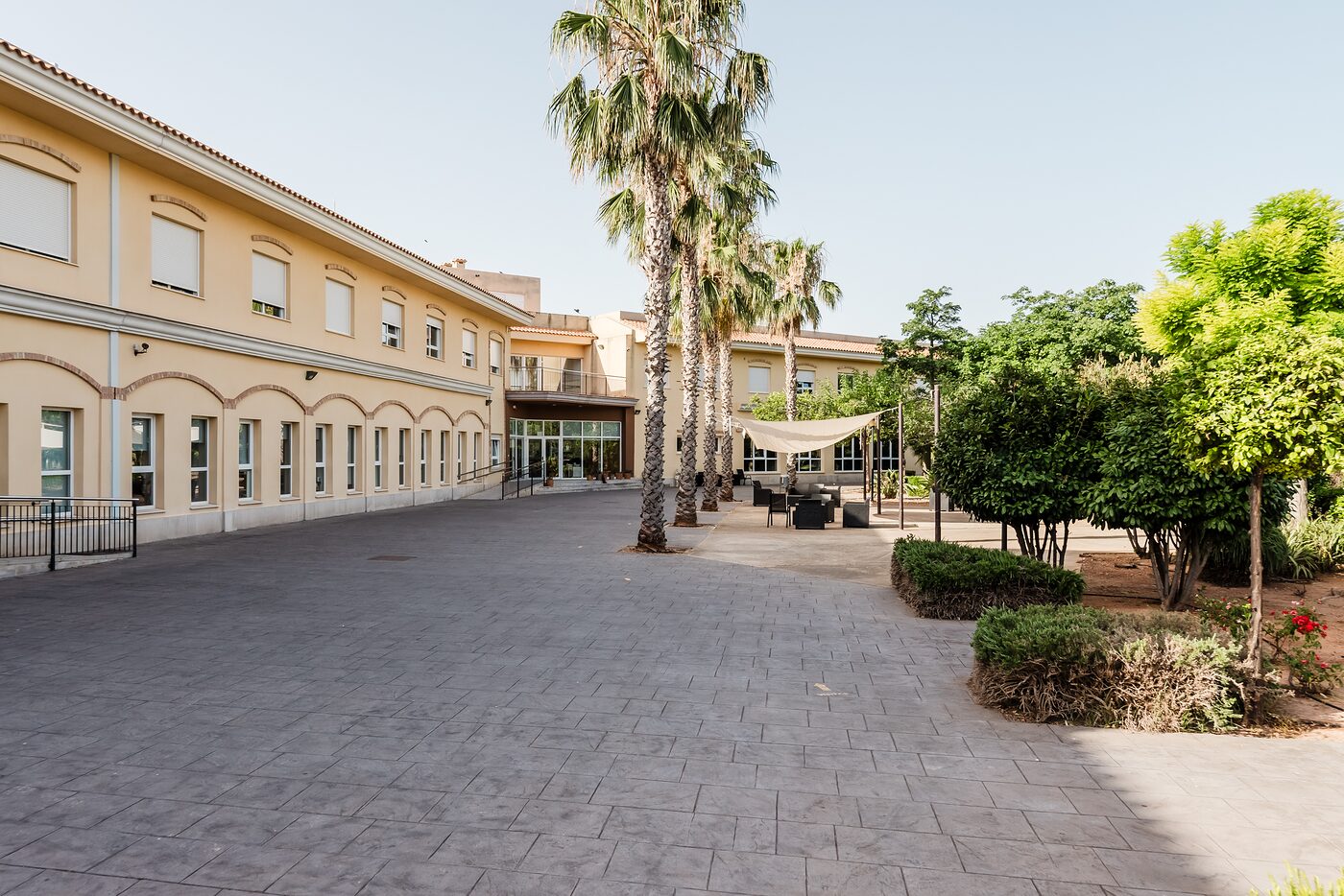Fachada mediterránea con palmeras, explanada y jardines